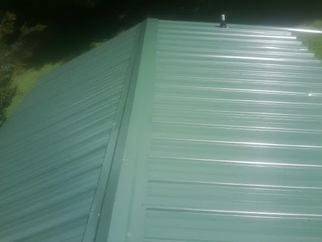 New green metal panels meeting at the ridge of a roof — Flat Roof Repair work by our crew in Sharon