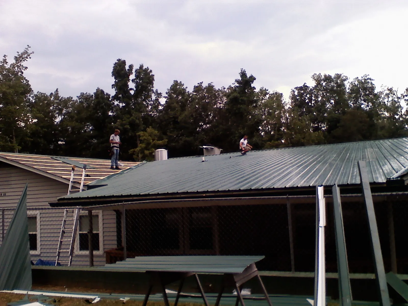 Two roofers installing green metal panels above a covered porch in Sharon
